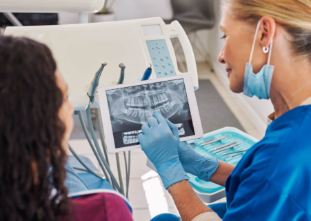 Dentist reviewing a panoramic dental X-ray with a patient to identify cavities and explain what tooth decay looks like on an X-ray.